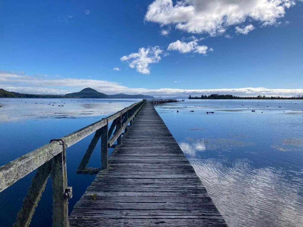 un muelle de madera se extiende sobre un cuerpo de agua en Kiwi cabin with geothermal pool by lake Taupo en Turangi