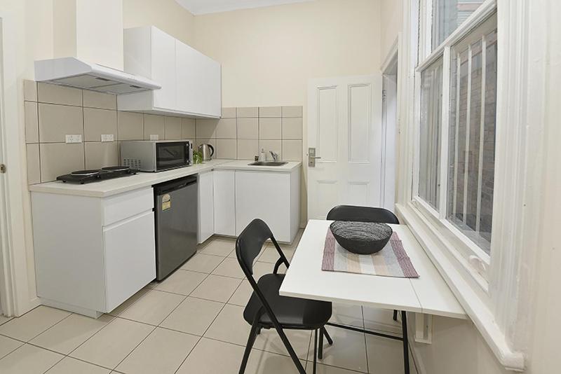 een witte keuken met een tafel en 2 stoelen bij 51CR3 - Lovely One Bedroom Apt Next to RMIT! AC, 50incTV in Melbourne