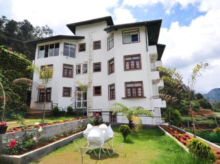 una grande casa bianca con due sedie in cortile di New Ashley Resorts (PVT) LTD a Nuwara Eliya