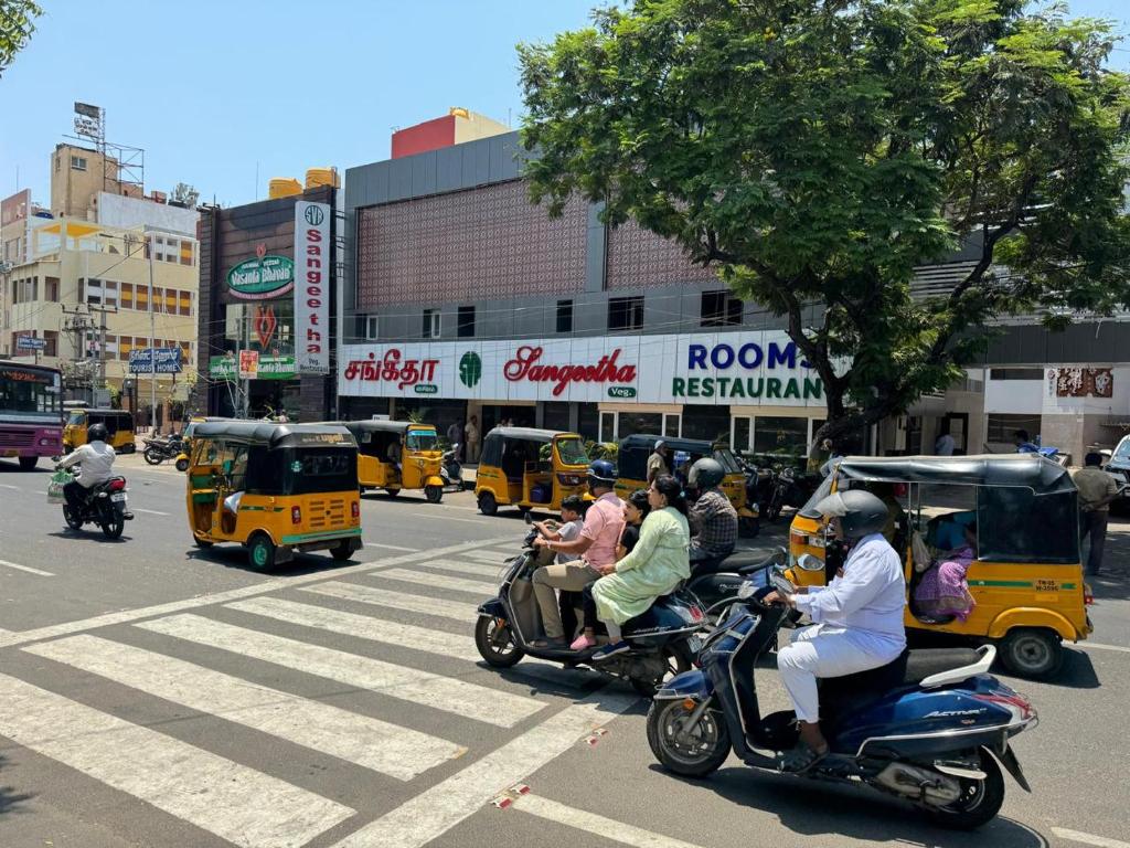 un grupo de personas montando scooters en una concurrida calle de la ciudad en Sangeetha Business Hotel, en Chennai