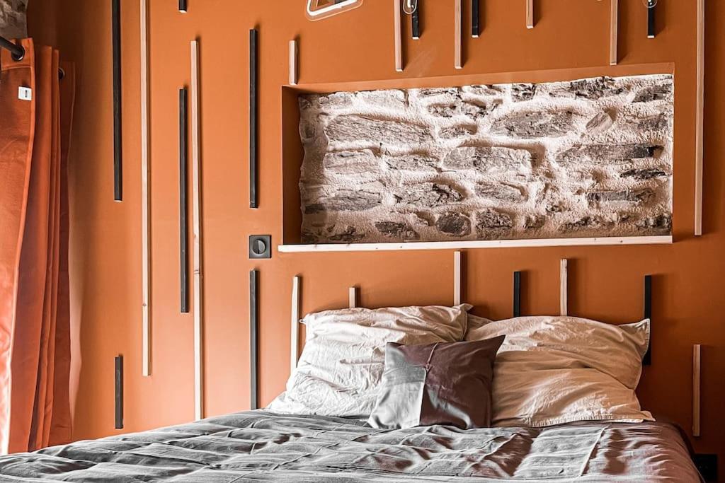 Una cama con una pared de color naranja con una foto encima. en Le Four' Nid, en La Terrasse-sur-Dorlay