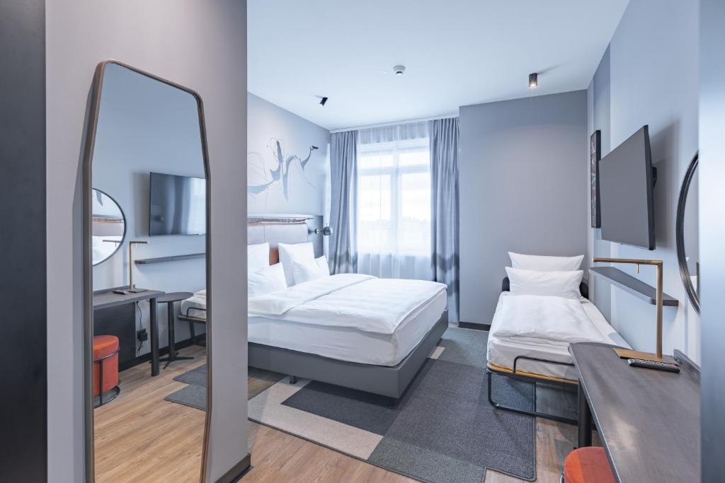 Habitación de hotel con cama y espejo en TITANIC Comfort Kurfürstendamm, en Berlín