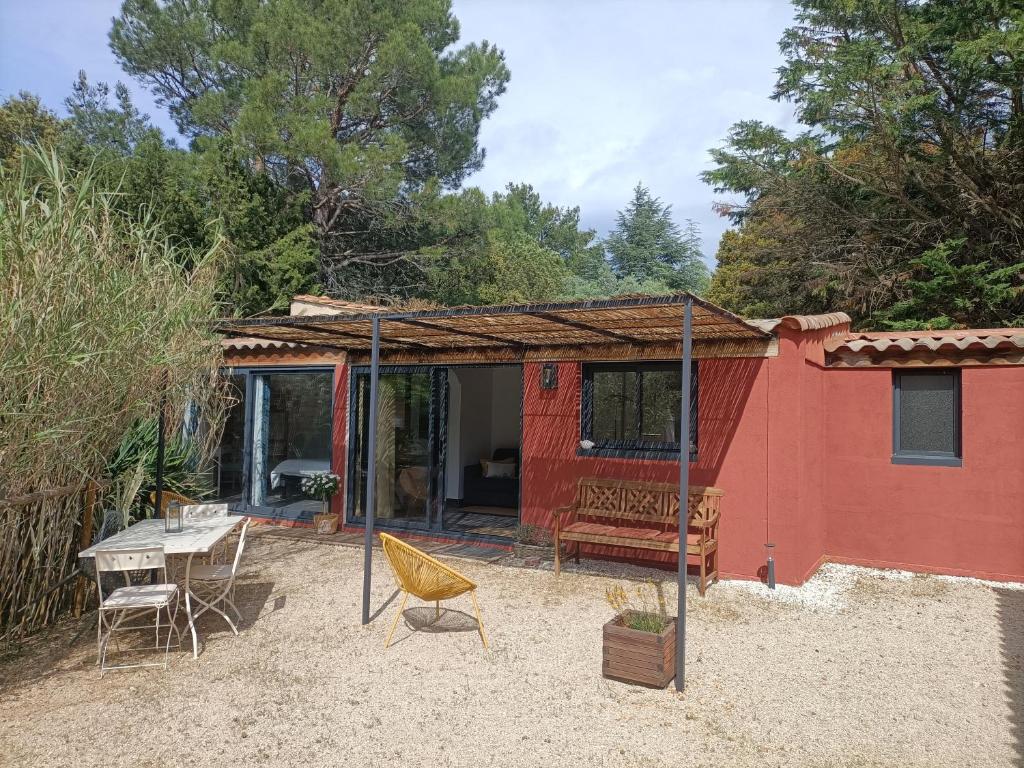 een rood huis met een tafel en stoelen in het zand bij Maisonnette tout confort in Rochefort-du-Gard