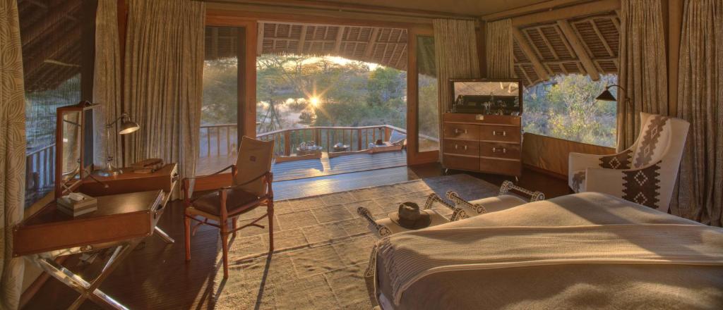 a bedroom with a bed and a desk and a balcony at Finch Hattons Luxury Tented Camp in Tsavo