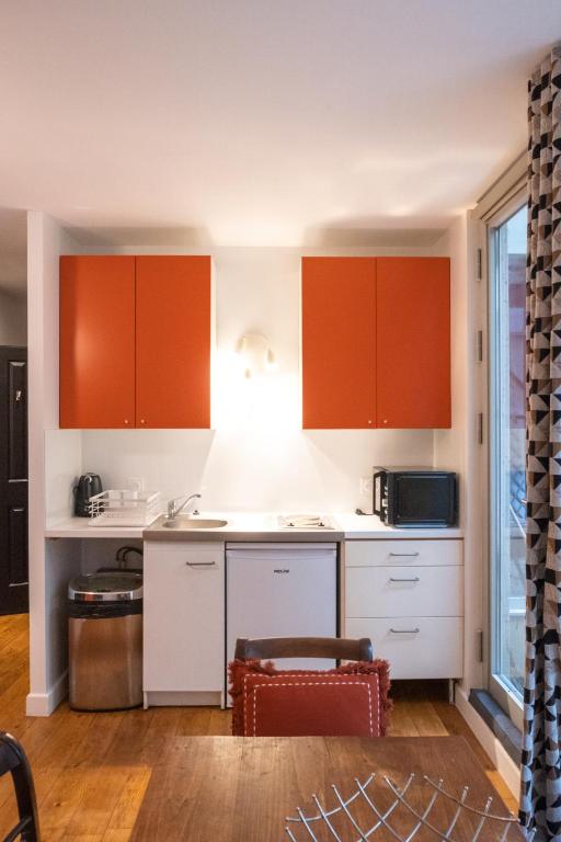 une cuisine avec des armoires orange et des comptoirs blancs dans l'établissement studio d'ALO, à Clamart
