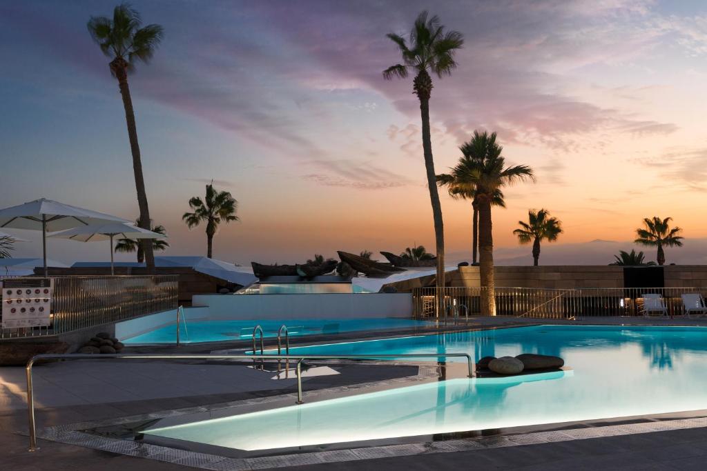 two swimming pools with palm trees in the background at La Isla y el Mar, Hotel Boutique in Puerto del Carmen