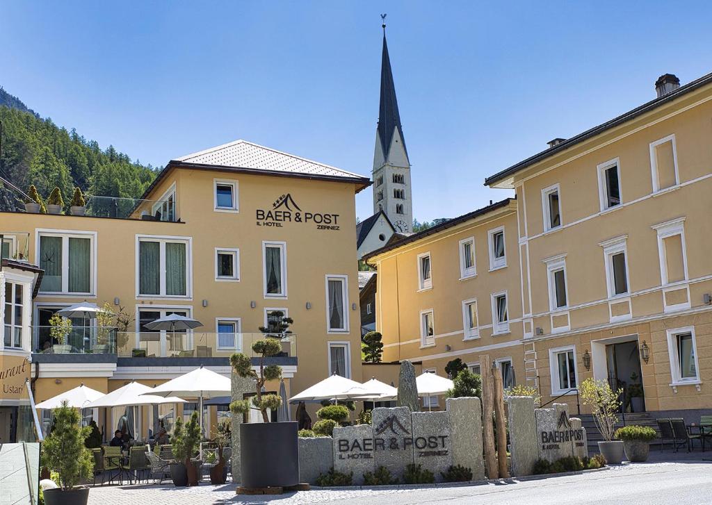 un groupe de bâtiments avec des parapluies et une église dans l'établissement Hotel Baer & Post Zernez, à Zernez