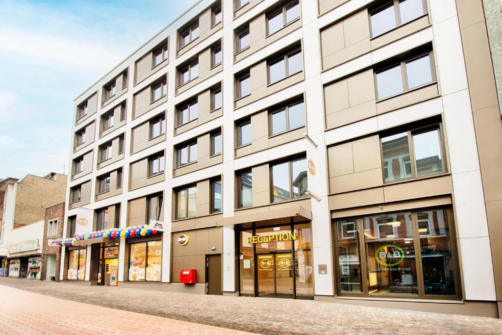 a large white building on a street with shops at B&B Hotel Aachen-City in Aachen