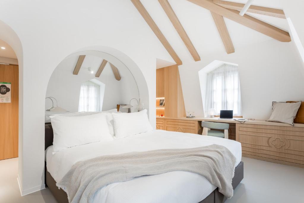 a white bedroom with a large bed and a desk at Hôtel de La Cigogne in Saint-Ursanne