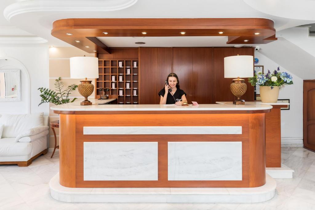 a woman sitting at a bar in a lobby at Eliza Hotel by Panel Hospitality - Formerly Evdion Hotel in Nei Poroi