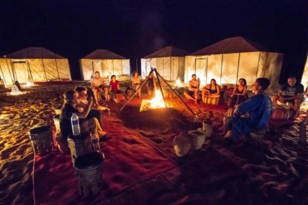 a group of people sitting around a camp fire at Sunset Camp Merzouga in Merzouga