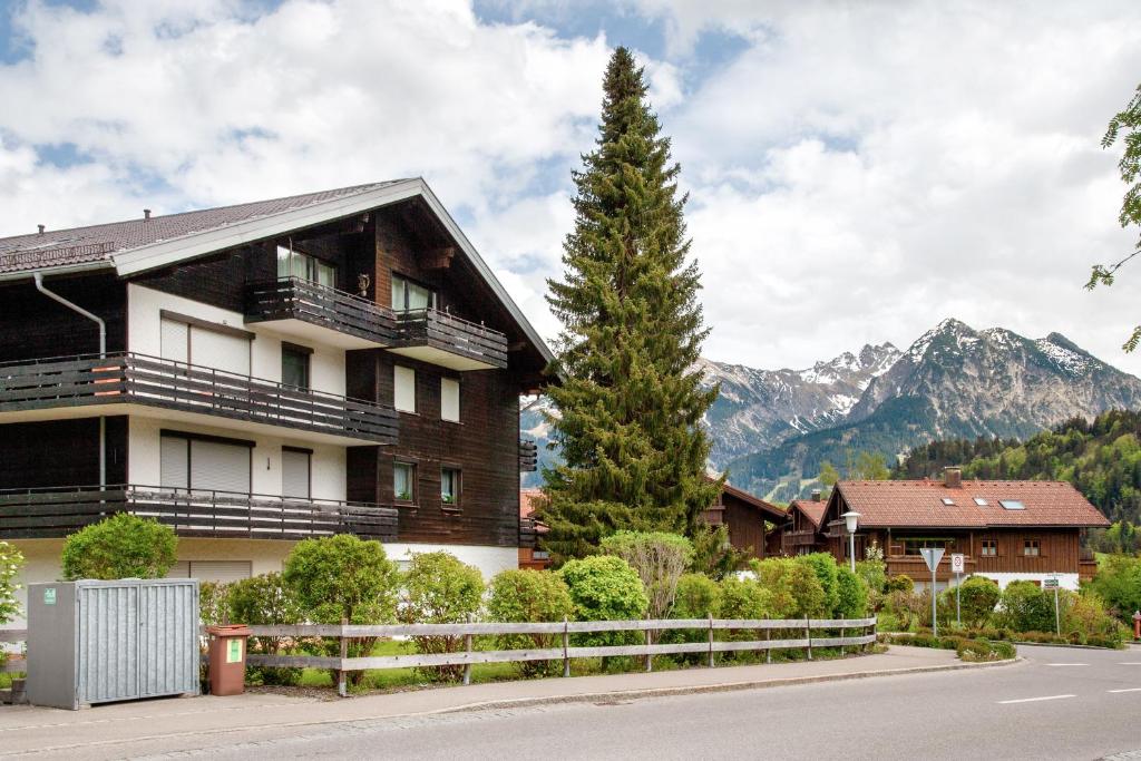 un bâtiment avec un arbre et des montagnes en arrière-plan dans l'établissement Ferienwohnung Bergrose, à Obermaiselstein