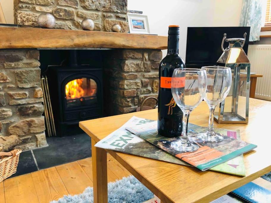 a bottle of wine and two glasses on a table with a fireplace at Stables A delightful one bed cottage with parking! in Appledore