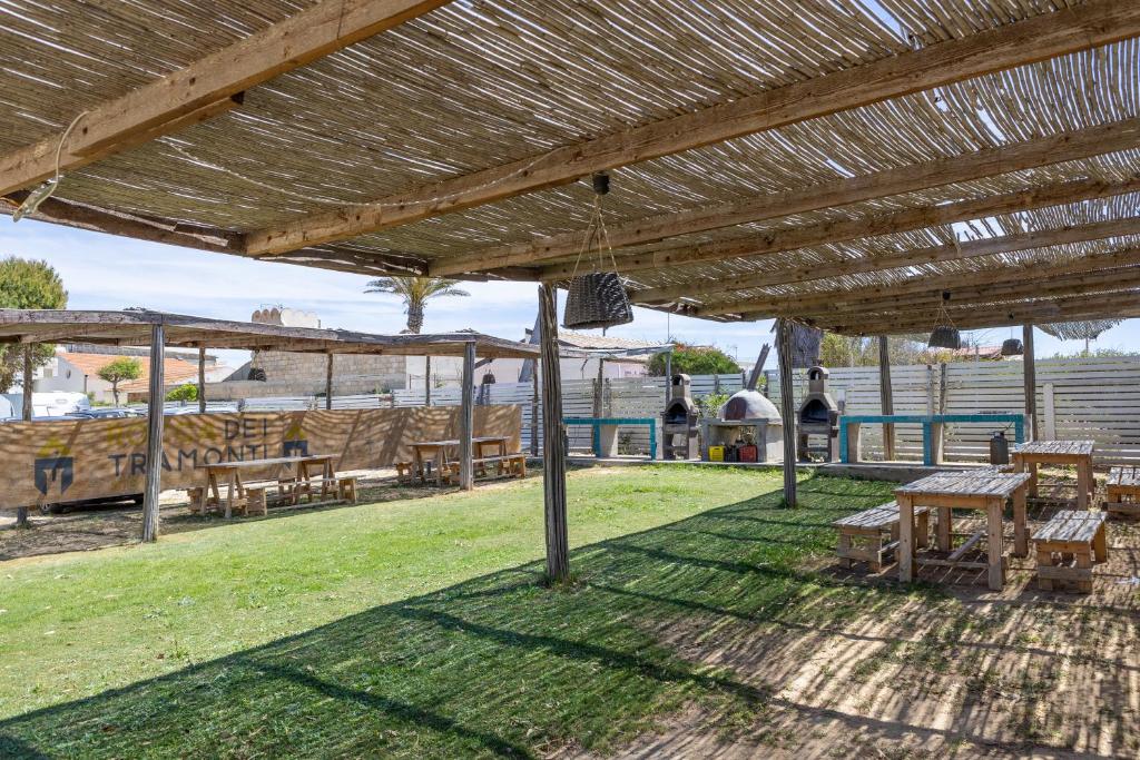 eine Terrasse mit Tischen und Bänken unter einem Holzdach in der Unterkunft Rocca dei Tramonti Apartments in Punta Braccetto