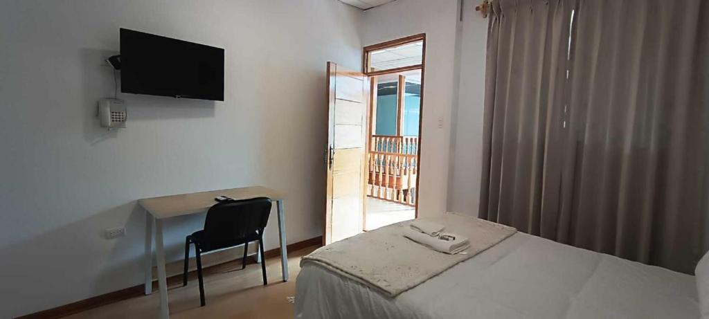 een slaapkamer met een bed, een bureau en een televisie bij Hotel Aural in Cajamarca