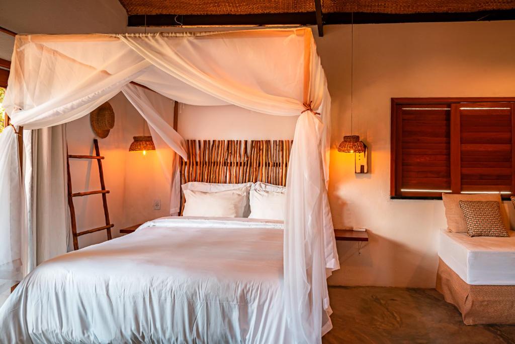 a bedroom with a canopy bed with white sheets and pillows at Paka Bangalos, Pousada de Charme em Sergipe in Pacatuba