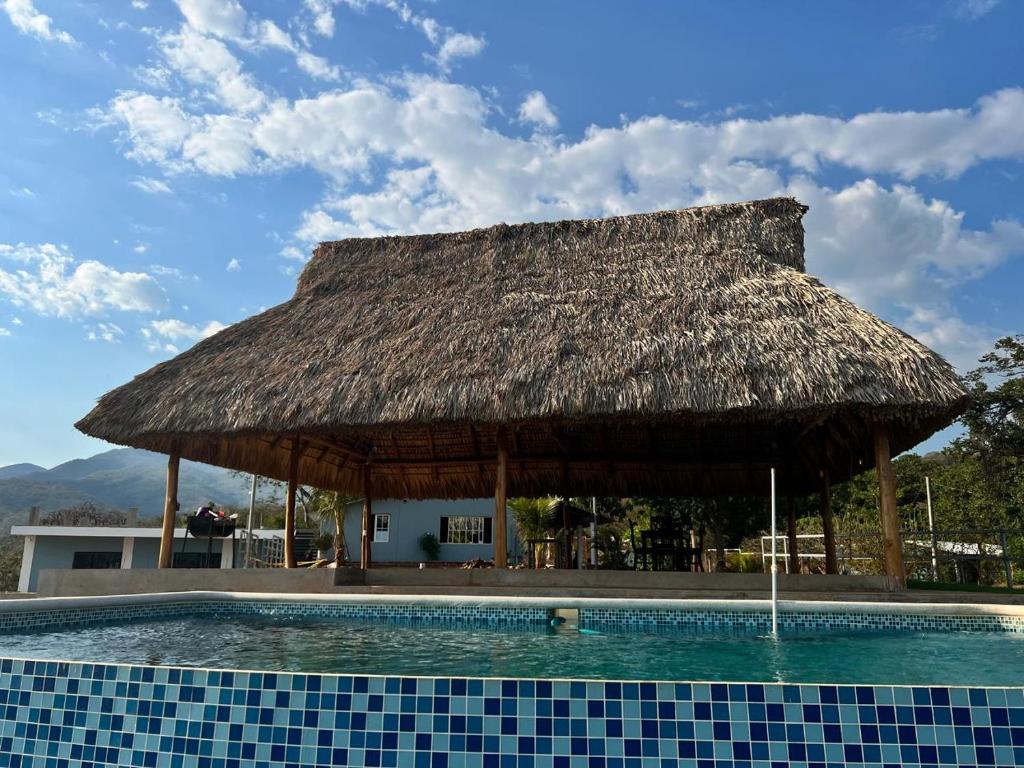 een hut met een zwembad met een rieten dak bij Rancho Agua Fria casa in Usulután