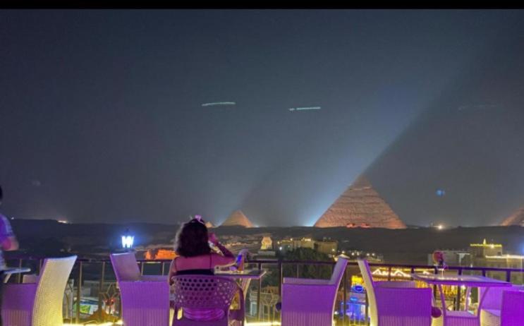 Royal Golden Pyramids Inn في القاهرة: امرأة جالسة على كراسي أرجوانية تطل على الأهرامات