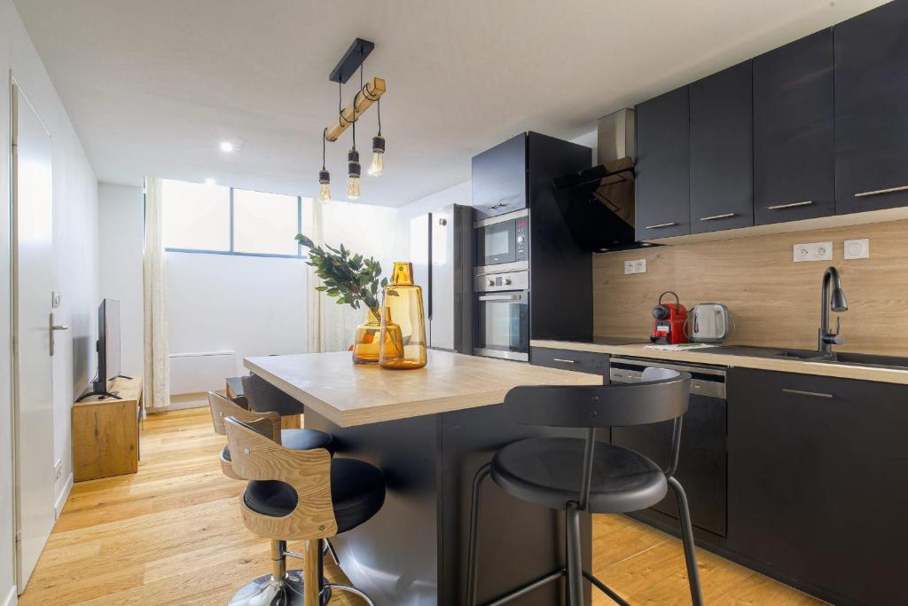 une cuisine avec des placards noirs et un comptoir avec des tabourets de bar dans l'établissement Cosy et Charmant wifi très haut débit, à Lyon