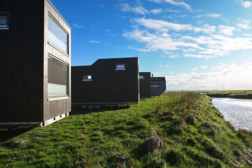 a row of black houses on the side of a river at Tiny House Nature 14 Zur Meerseite - Green Tiny Village Harlesiel in Carolinensiel