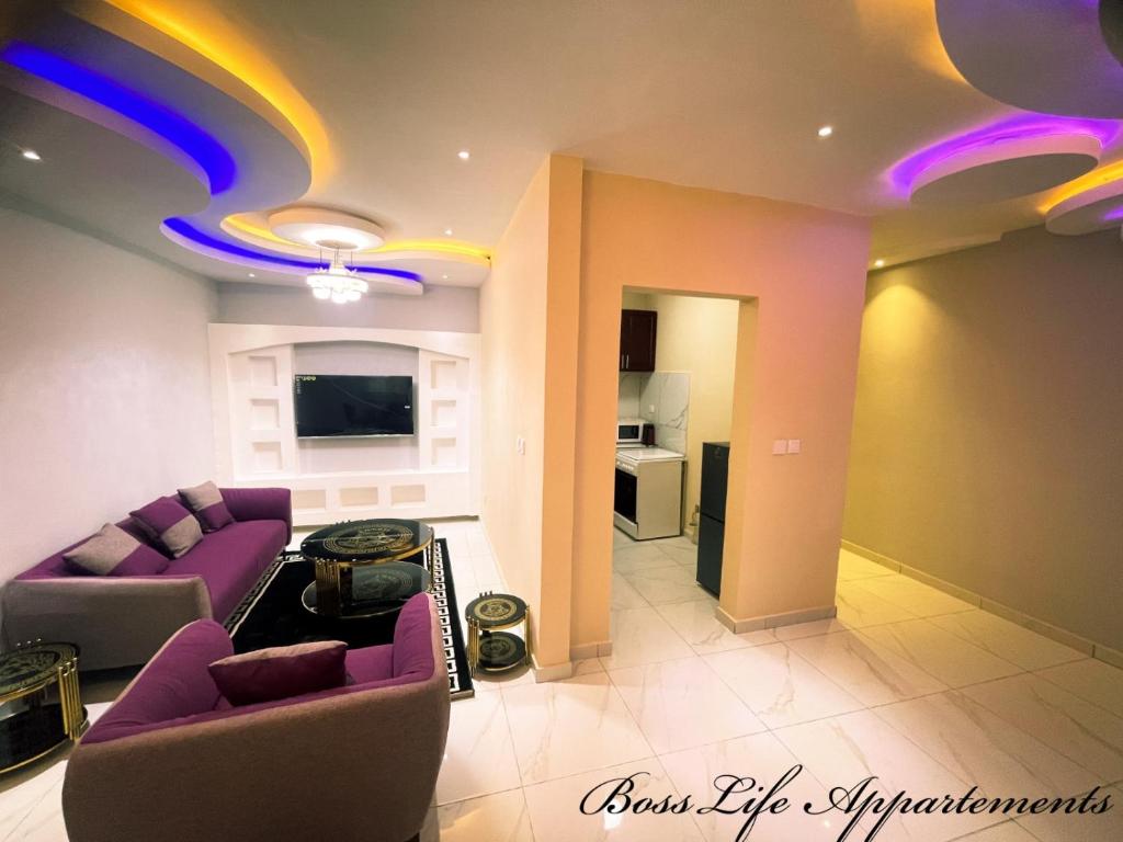 uma sala de estar com sofás roxos e uma cozinha em BOSSLIFE APARTMENTS-TERMINUS SAINT MICHEL DERRIERE Barcelone Hôtel em Douala