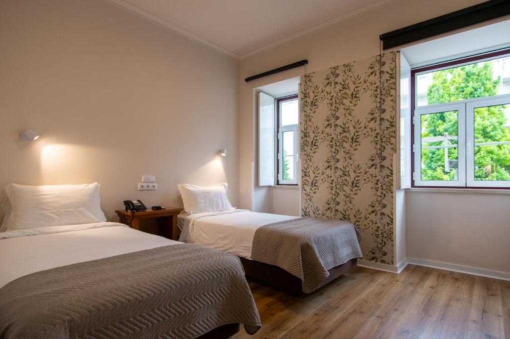 two beds in a room with two windows at Hotel Vitória in Coimbra