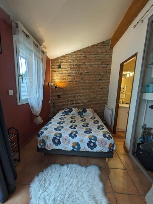 une chambre avec un lit et un mur de briques dans l'établissement un cocon de briques Rose, à Rouffiac-Tolosan