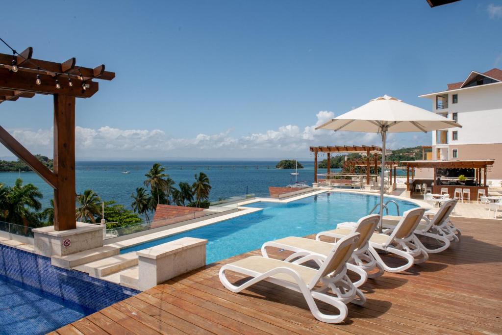 una piscina con sillas y una sombrilla y el océano en Hacienda Samana Bay Hotel en Santa Bárbara de Samaná