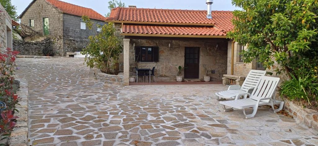 un patio con 2 sillas blancas y una casa en Casa da Rosa Porreiras, en Paredes de Coura