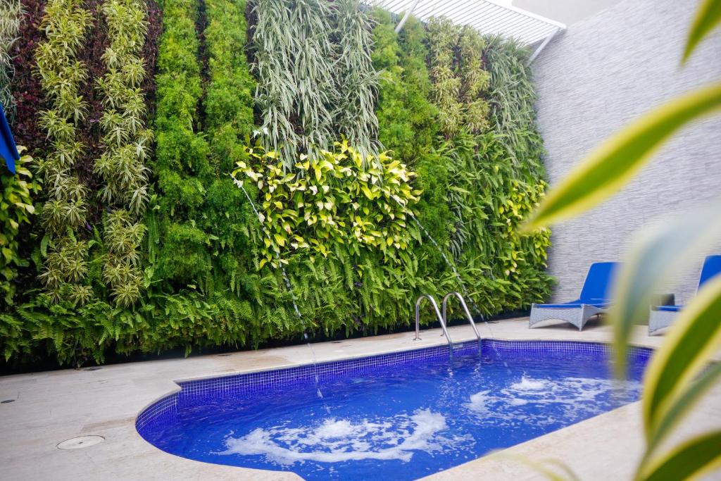 una piscina en un patio trasero con una pared verde en Varanasi Hotel Boutique Aeropuerto en Cartagena de Indias
