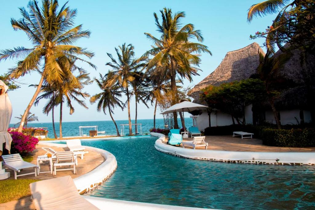 een zwembad van het resort met palmbomen en de oceaan bij MARIA the Star on the Sea Beach cottages, cottage Mama in Malindi