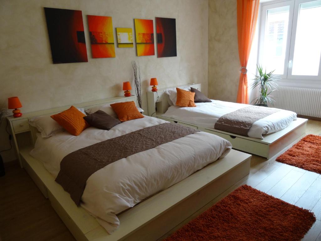 ポマールにあるCes Jours À Pommardのオレンジ色のカーテンとオレンジ色のラグが備わるベッドルームのベッド2台