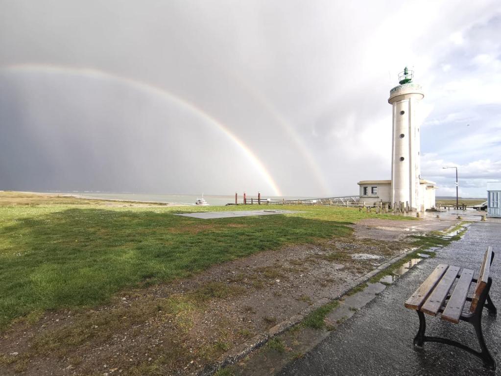 un arco iris sobre un faro con un banco al lado en Le Gîte du Phare vue sur mer en Cayeux-sur-Mer