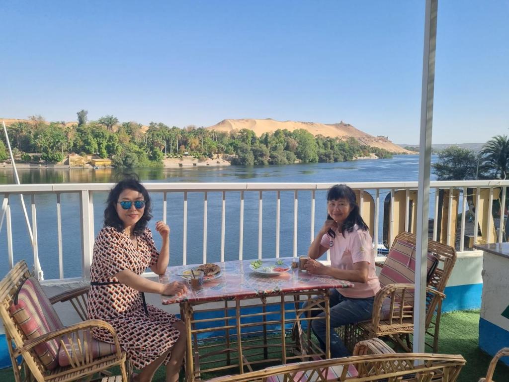 two women sitting at a table on a balcony overlooking a river at ABAZIDO Nubian Guest House in Aswan