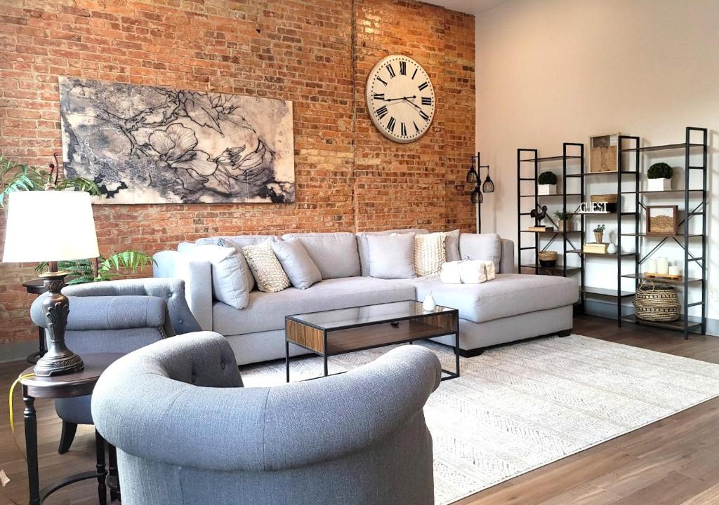 a living room with a couch and a clock on a brick wall at Spacious luxury apt in Historic Downtown - OH Amish country in Millersburg