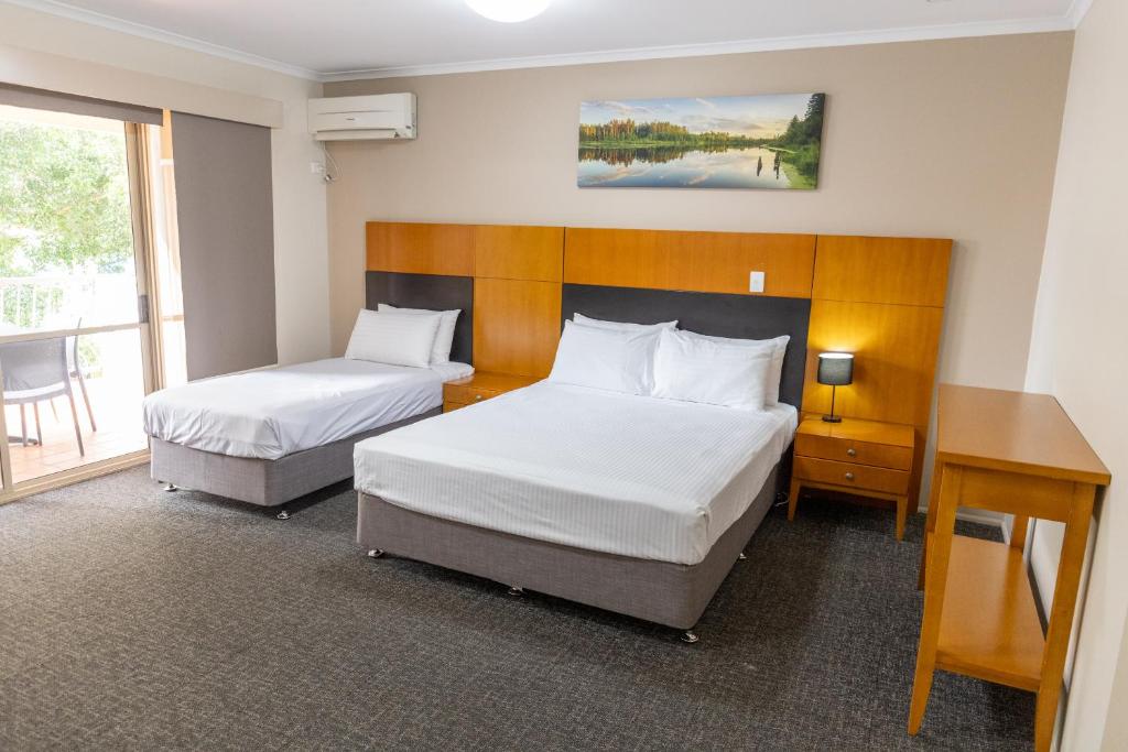 a hotel room with two beds and a desk at Sundowner Hotel Motel in Caboolture