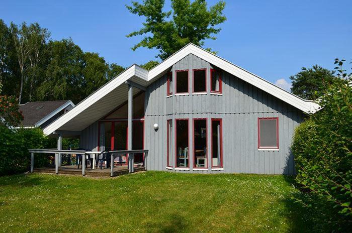uma casa cinzenta com acabamento vermelho num relvado verde em Wildgans 80 em Mirow