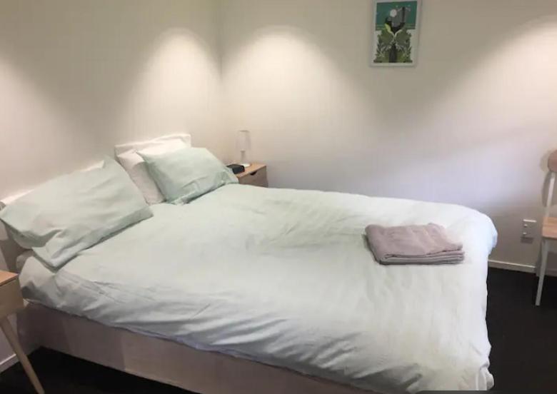 Una cama con sábanas blancas y una toalla rosa. en Kingsland Studio - Walk to Eden Park! en Auckland