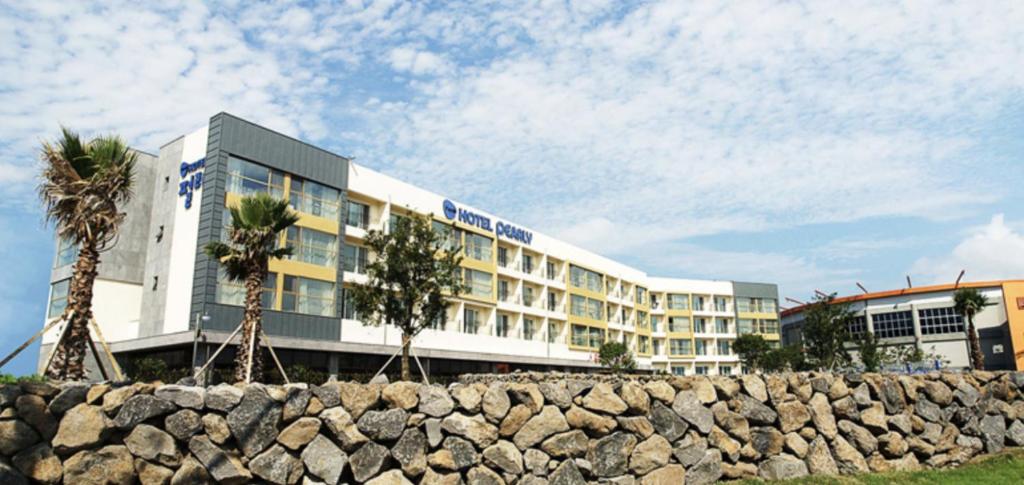 un hotel con palmeras frente a una pared de piedra en Pearly Hotel en Jeju