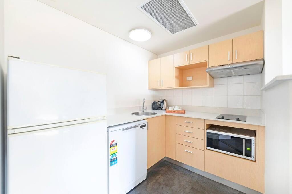 a kitchen with wooden cabinets and a white refrigerator at Idyllic Waterfront Pool Escape with Esplanade View in Darwin