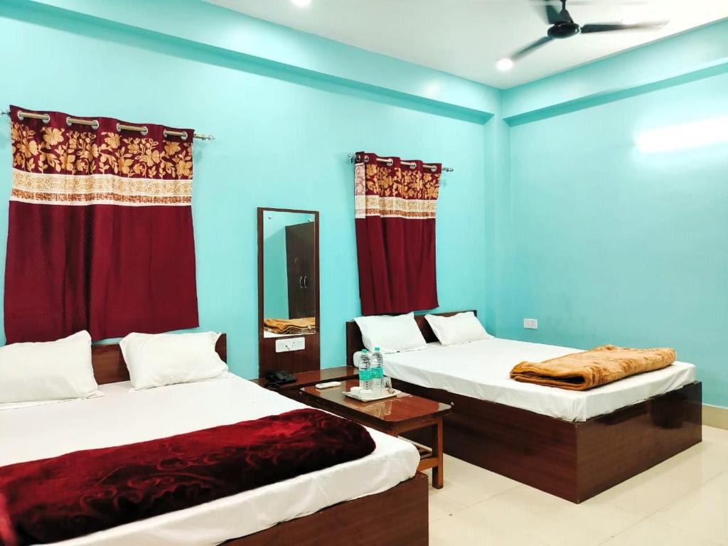 2 Betten in einem Zimmer mit blauen Wänden und roten Vorhängen in der Unterkunft Hotel Ambika in Deoghar