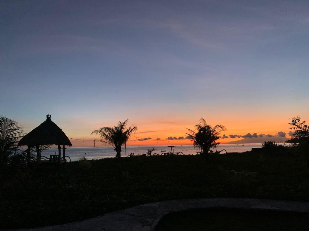 un tramonto sull'oceano con un gazebo e palme di Yogi Beach Cabin ad Amed