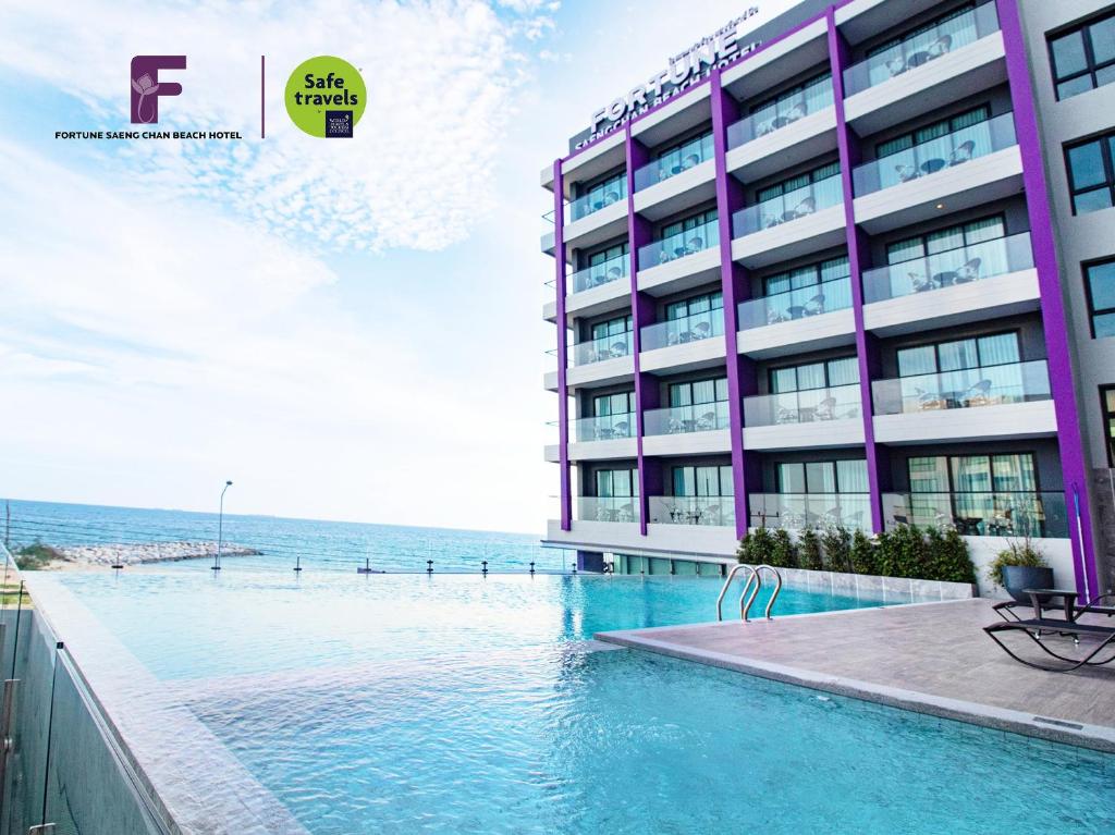a hotel with a swimming pool in front of a building at Fortune Saeng Chan Beach Hotel Rayong - SHA Plus in Rayong
