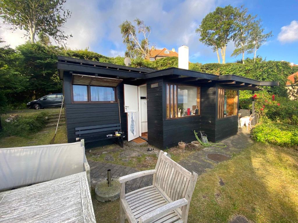 ein schwarzes winziges Haus mit einer Bank davor in der Unterkunft Cozy Summer House In The First Row To The Water, in Hornbæk