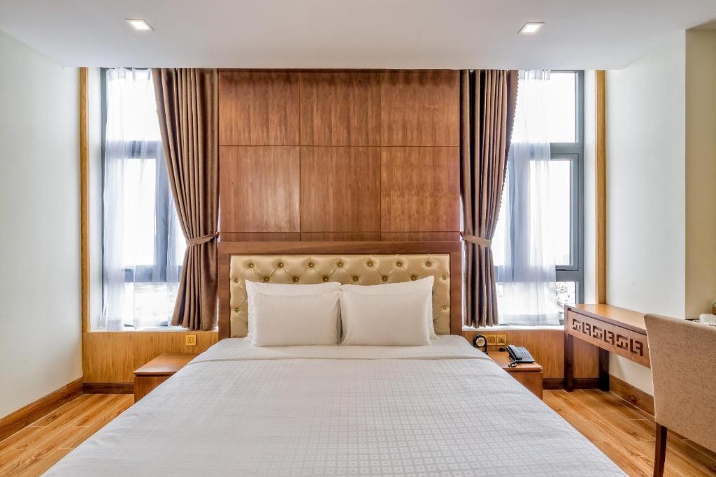 A symmetrical bedroom with a large bed between two curtained windows and a compact desk.
