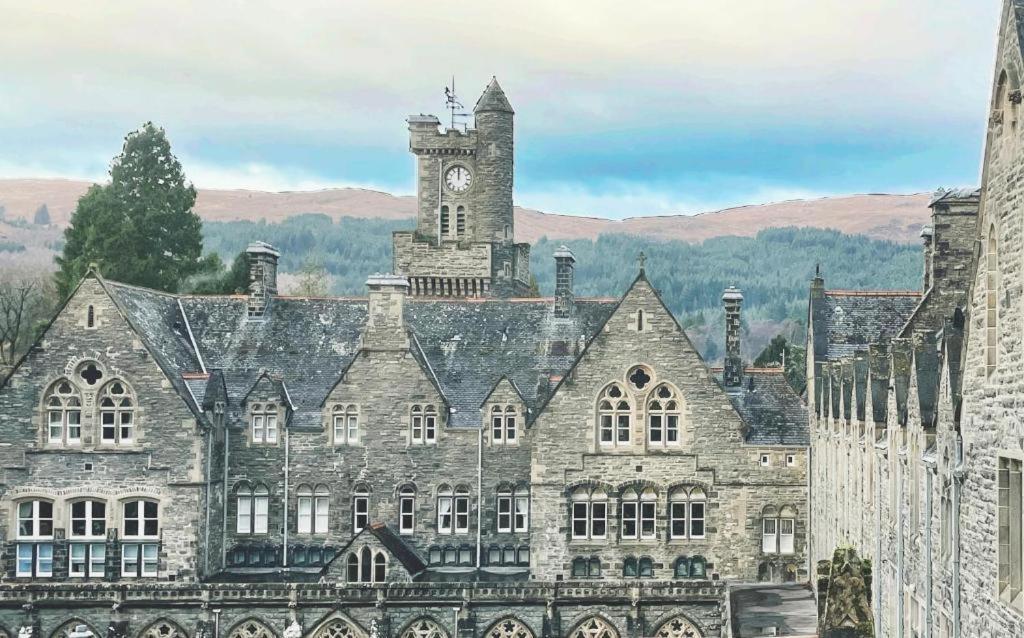 un antiguo edificio con una torre de reloj encima en The Classrooms, Loch Ness Abbey - 142m2 Lifestyle & Heritage apartment - Pool & Spa - The Highland Club - Resort on lake shores, en Fort Augustus