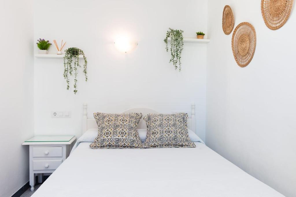 a white bedroom with a bed and plants on the wall at Hostal Restaurante La Giralda in Rota