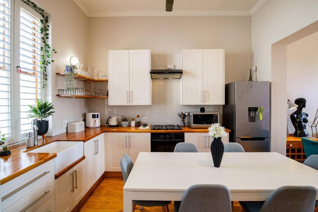 uma cozinha com armários brancos e uma mesa com cadeiras em Quirky 2 Bed Home Parking Wi-Fi Backup Power em Cidade do Cabo