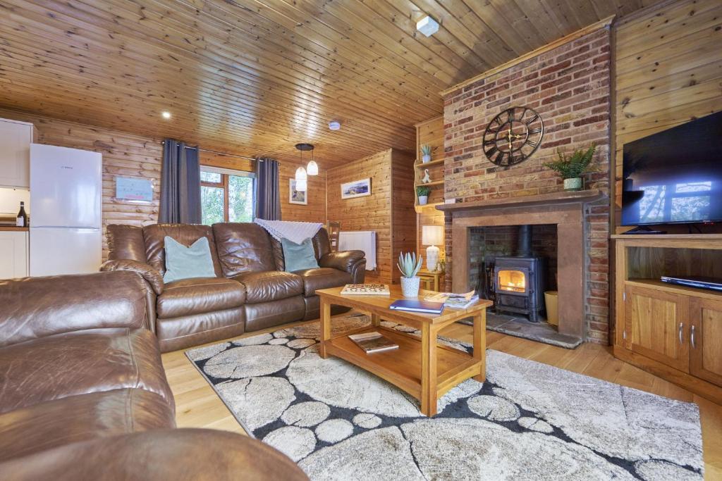 a living room with a leather couch and a fireplace at Dunnock Lodge with Hot-tub in Carlisle