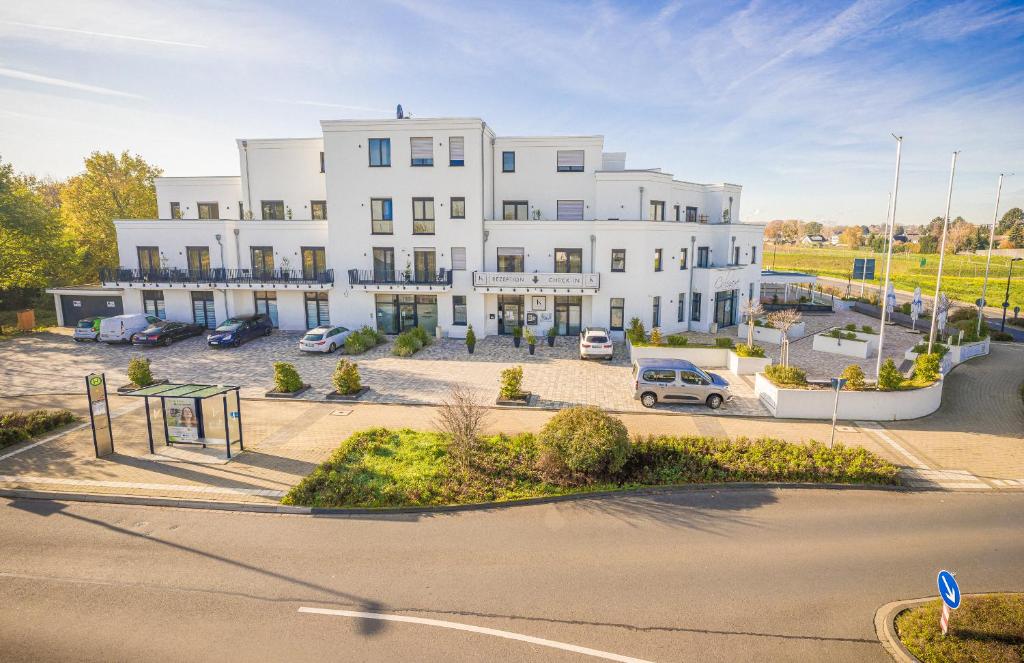 een groot wit gebouw met auto's geparkeerd op een parkeerplaats bij K-Apart Hotel & Boardinghouse in Hürth